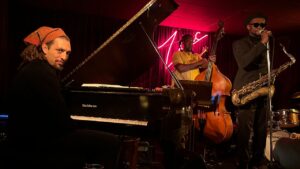 Mathis Picard plays piano and saxophone in front of a band, showcasing his musical talent and engaging with the audience.